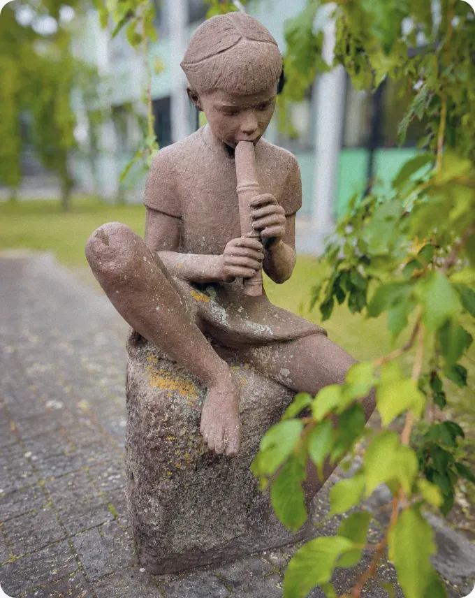 Stenskulptur af et barn med en fløjte i skolegården på Brøndbyvester Skole.