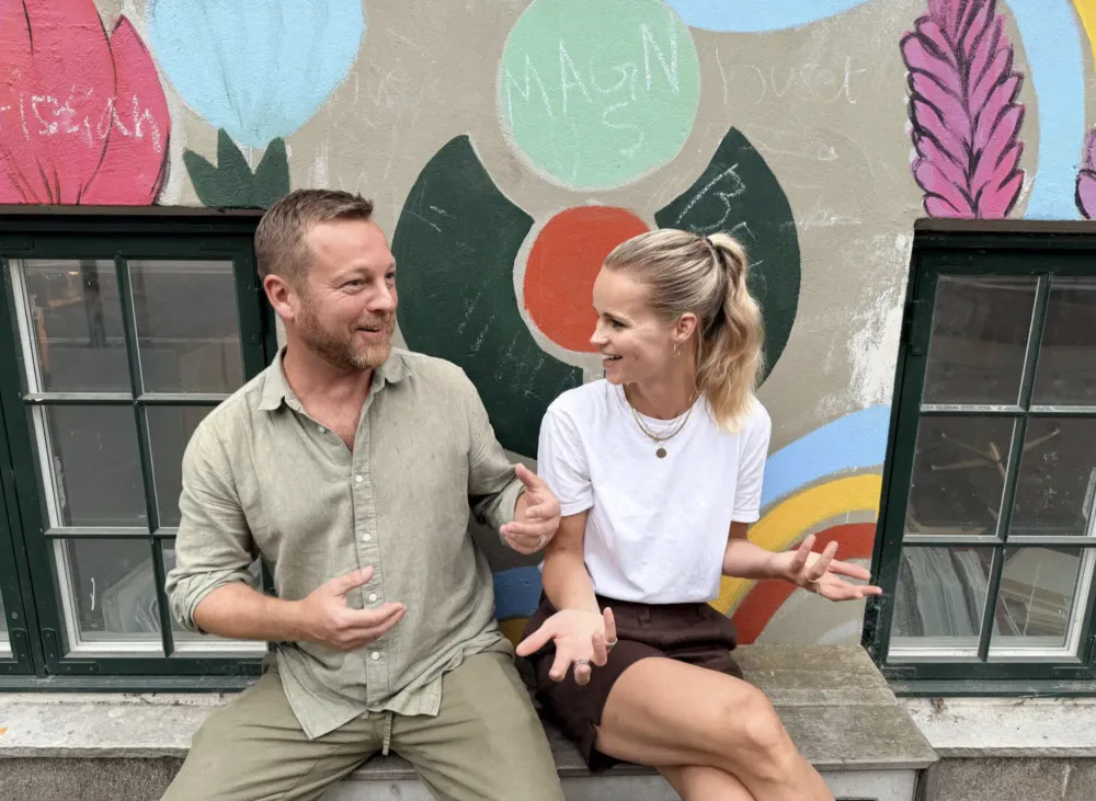 Skoleleder Lars Westh og souschef Sabine Skafte sidder på en bænk foran en bemalet mur i skolegården.